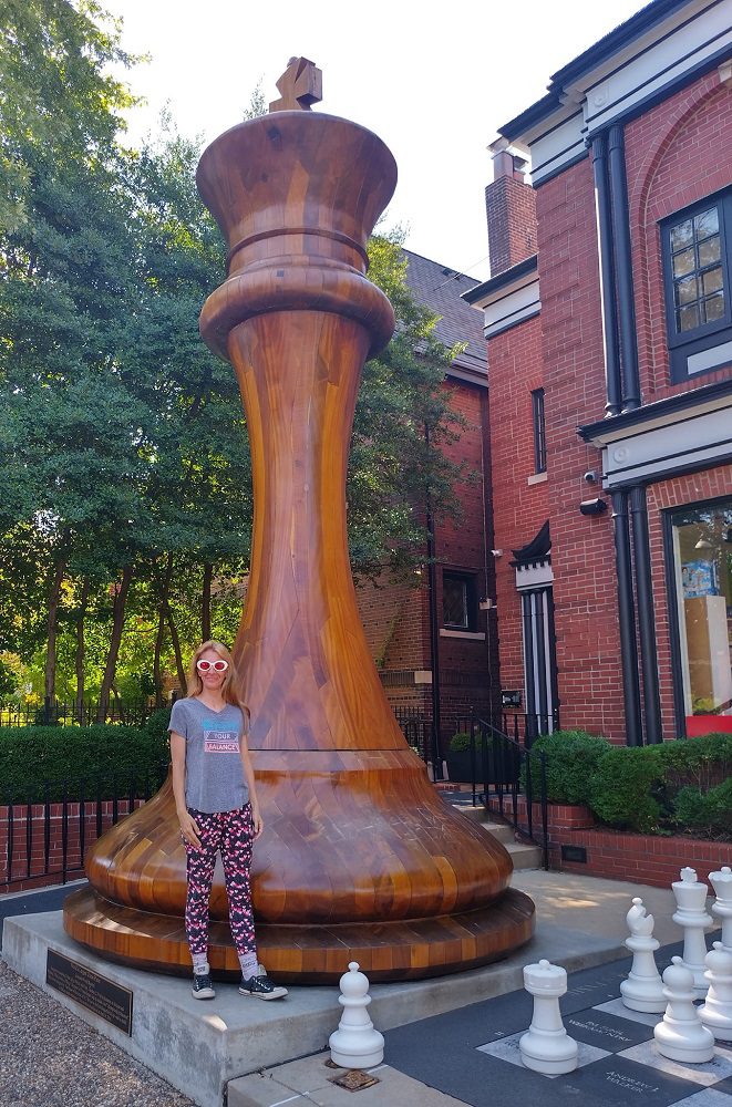 Visitor standing next to the World's Largest Chess Piece in St Louis - a 20-foot mahogany King outside the World Chess Hall of Fame