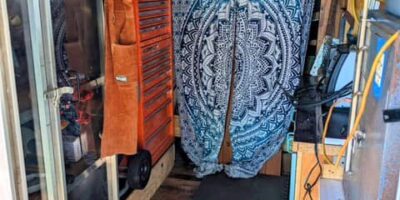 Small organized tool area inside converted bus—orange tool chest, hanging storage, and curtain leading to workshop nook.