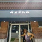 Exterior view of Refab St Louis Repurpose Shop, showing a person standing near the entrance of the brick building with a black awning that displays the shop’s name in white lettering