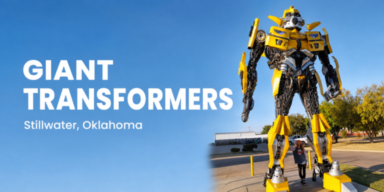 Nancy stands beneath the towering yellow Bumblebee statue in Stillwater, Oklahoma, beside the words “Giant Transformers — Stillwater, Oklahoma.”