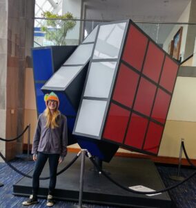 Person standing in front of the world’s largest Rubik’s Cube inside the Knoxville Convention Center, showcasing the sculpture’s playful tilt and bold colors.