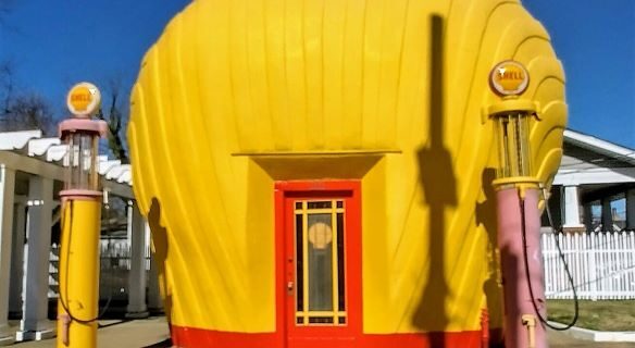 The Last Shell-Shaped Shell Service Station, a bright yellow building designed like a giant seashell, with two vintage pastel gas pumps and a red door