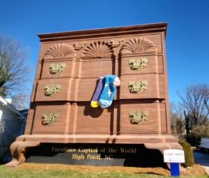 The World's Largest Chest of Drawers towering over the street in High Point, North Carolina, with a pair of colorful socks hanging from an open drawer—a playful nod to the city's furniture industry.  One of the many Weird things to do in North Carolina