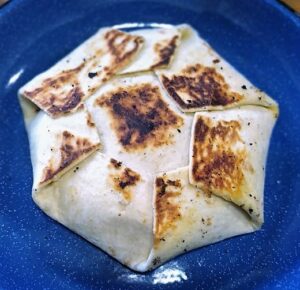 Grilled Crunchwrap Supreme Copycat folded into a hexagon with visible sear marks on top, served on a blue plate as the final toasted version of the copycat recipe.