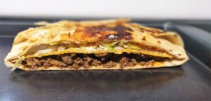 Close-up of a folded and grilled Crunchwrap with golden-brown edges, showing a hint of seasoned ground beef inside the toasted tortilla.