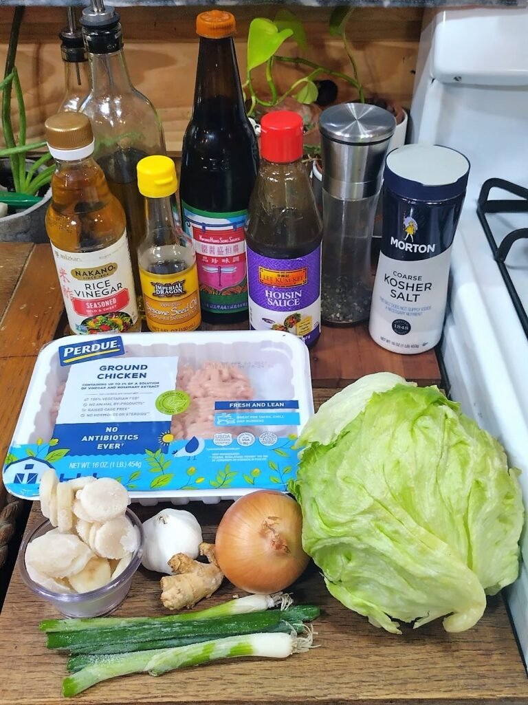 Cooking ingredients on a counter including sauce bottles, a package of ground chicken, a head of lettuce, an onion, and green onions