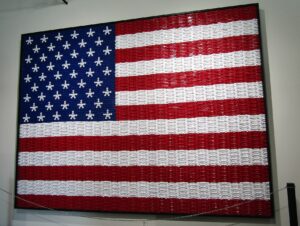 American flag constructed entirely from rows of red, white, and blue plastic kazoos arranged on a black wall—thirteen stripes and a star field recreated with kazoo chaos and patriotic commitment.