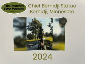 2024 photo of the Chief Bemidji Statue in Bemidji, Minnesota, with a person holding a child nearby on a sunny day in the park