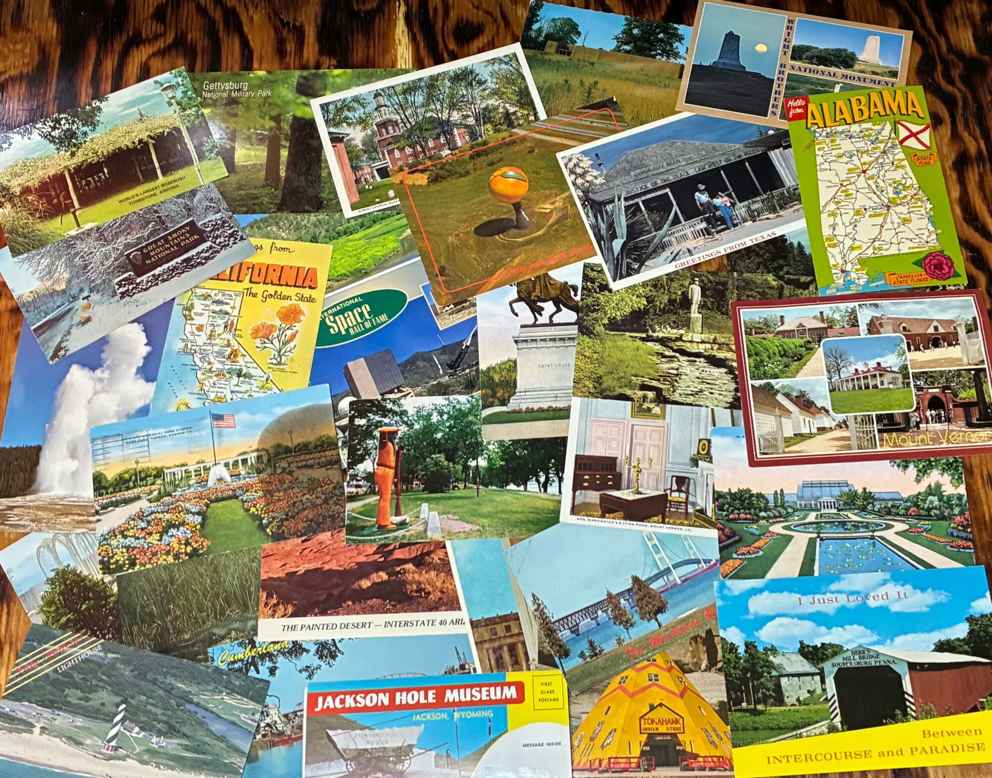 Collection of vintage postcards spread on wooden table featuring roadside attractions and travel destinations
