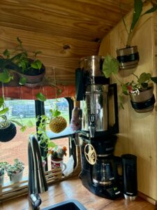Coffee station surrounded by hanging and potted plants on a converted school bus