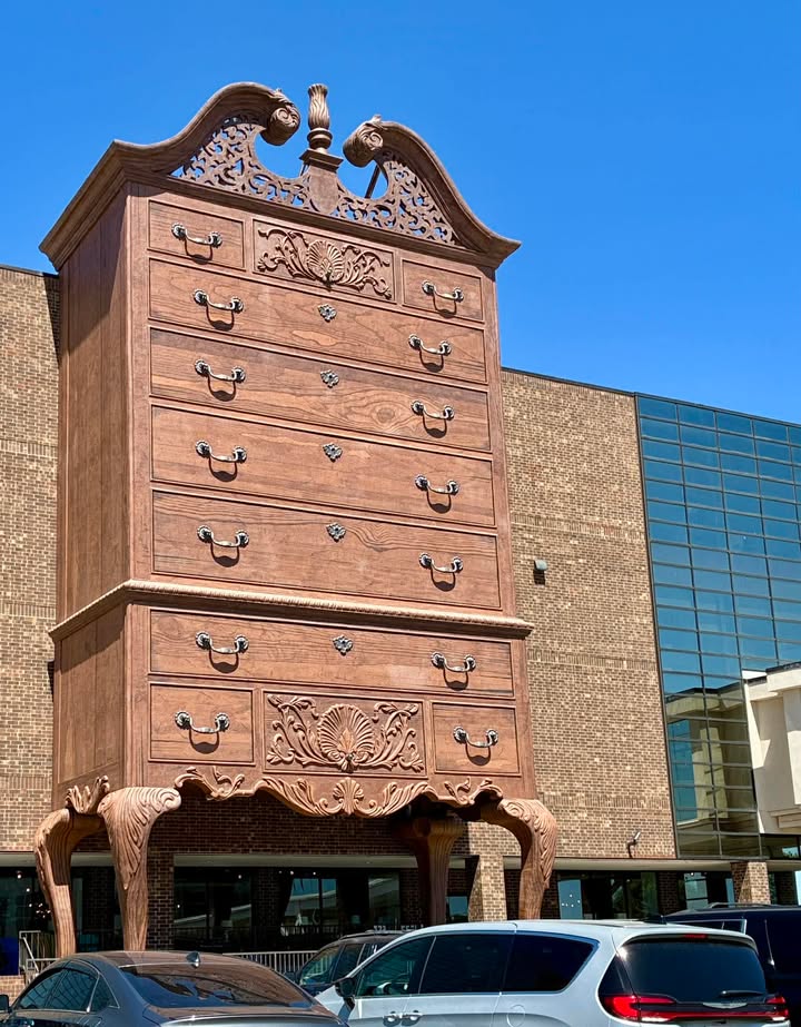 Close-up of the World's Largest Highboy Dresser's drawers and ornate broken pediment top, with parked cars and the Furnitureland South building below