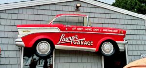 Red 1957 Chevrolet Bel Air pickup truck mounted above the entrance to Lawyer Garage in Virginia Beach, Virginia, with "Art Cars, Movie Cars & Awesomeness" painted along the side.