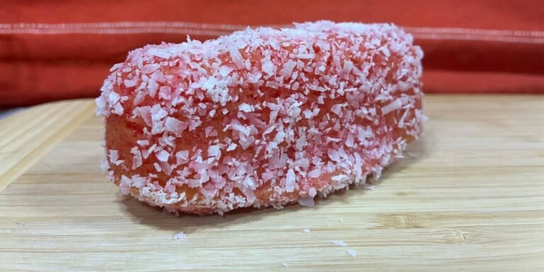 A homemade pink coconut-covered cake on a wooden cutting board