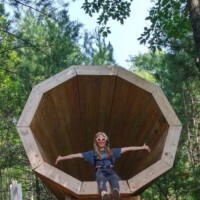 Nancy inside the wooden megaphone sculpture at Agnes Andreae Nature Preserve Michigan — arms outstretched, forest backdrop, July hike moment