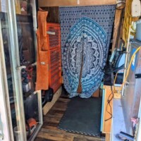 Small organized tool area inside converted bus—orange tool chest, hanging storage, and curtain leading to workshop nook.