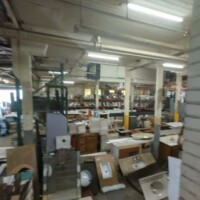 Interior of Refab St Louis Repurpose Shop showcasing a cluttered but resource-rich warehouse space filled with sinks, cabinets, countertops, and other reclaimed fixtures arranged along metal racks and shelves beneath fluorescent lighting.