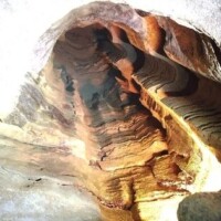 Inside War Eagle Cavern Arkansas, curved bands of brown, orange, and beige rock sweep across the walls, lit to reveal every layered contour.