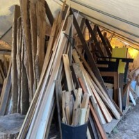 Outdoor lumber storage area at Refab St Louis Repurpose Shop featuring a variety of reclaimed wood pieces stacked under a canopy structure, including long planks, shorter boards, and irregular cuts organized for salvage and reuse projects.