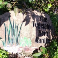 Stone sign for the Vegetable Herb Garden at the Botanical Garden of the Ozarks, surrounded by green foliage and painted herb illustrations