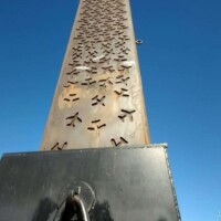 Large outdoor sculpture, mounted on a black base with a decorative metal ring, photographed from a low angle against a clear blue sky — quirky public art near the Center of the Universe Tulsa.