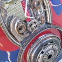 Assemblage of gears, clutch plates, and springs welded into a stylized face near the base of the Optimus Prime statue at G&M Body Shop in Stillwater, Oklahoma. Red and blue painted background ties into the robot’s color scheme. Part of the Transformers statues Stillwater Oklahoma roadside display.