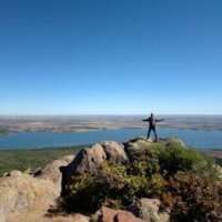Person standing triumphantly on Mount Scott summit overlooking lake and vast Oklahoma landscape
