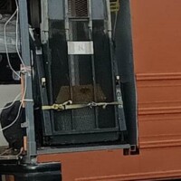 Heavy-duty lift attached to back deck of converted bus, secured by yellow strap, used for loading heavy items