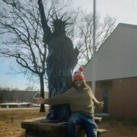 Person in a red cap sitting at the base of a Statue of Liberty replica