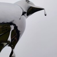 Close-up of the Reflection sculpture in Nashville—mirrored bird beak with a droplet, set against a cloudy sky.
