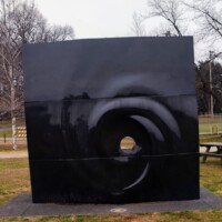 Reflection sculpture in Nashville’s Shelby Park—a geometric mirrored bird shape with a round cutout, placed near trees and a bench