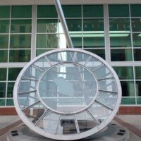 Large circular metal sundial sculpture in front of a glass building