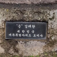 Black plaque with white Korean text embedded in a stone wall near the H.U. Lee International Gate in Little Rock; inscription credits Kim Tae-hwan, Governor of Jeju Special Self-Governing Province, Republic of Korea, marking the site as a formal cultural dedication.