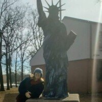 Replica of the Statue of Liberty on a pedestal with an American flag behind it