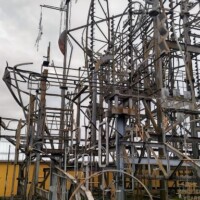 Vertical welded sculpture at Billy Tripp’s Mindfield Brownsville TN, built from rods, gears, coils, and mechanical parts, creating a dense outdoor installation against a yellow building and cloudy sky.