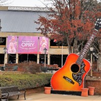 Colorful guitar sculpture in front of the Grand Ole Opry House in Nashville, Tennessee, with fall trees and performer banners in the background