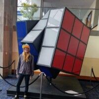 Person standing in front of the world’s largest Rubik’s Cube inside the Knoxville Convention Center, showcasing the sculpture’s playful tilt and bold colors.