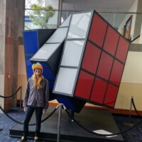 Person standing in front of the world’s largest Rubik’s Cube inside the Knoxville Convention Center, showcasing the sculpture’s playful tilt and bold colors.