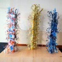 Three tall sculptures wrapped in vibrant orange, yellow, and blue materials, stacked on a wooden base inside the Knoxville Convention Center