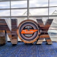 Wooden sculpture spelling “KNOX” with a circular Knoxville sign inside the “O,” and a statue of a figure on a pedestal beside it, framed by convention center windows