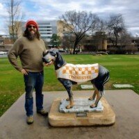 Man in a red cap standing beside a statue of a donkey wearing a checkered blanket