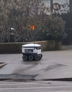 Small white six-wheeled delivery robot on a city sidewalk