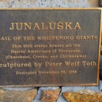 Dedication plaque for Peter Wolf Toth's 'Junaluska' Whispering Giant sculpture, part of the Trail of the Whispering Giants series, showing the sculpture details and 1976 dedication date in Johnson City, Tennessee