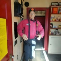 Inside The Last Shell-Shaped Shell Service Station: a life-sized statue of a man in a red shirt, dark pants, and suspenders stands near a red door with a yellow paper attached, alongside a shelf filled with books and memorabilia.