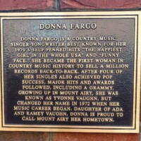 "A mounted plaque dedicated to country music singer-songwriter Donna Fargo, detailing her rise to fame with hits like 'The Happiest Girl in the Whole USA' and 'Funny Face.' The plaque highlights her achievements, including selling back-to-back million records and winning a Grammy, while proudly noting her roots in Mount Airy, North Carolina