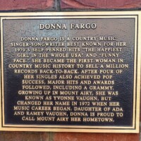 "A mounted plaque dedicated to country music singer-songwriter Donna Fargo, detailing her rise to fame with hits like 'The Happiest Girl in the Whole USA' and 'Funny Face.' The plaque highlights her achievements, including selling back-to-back million records and winning a Grammy, while proudly noting her roots in Mount Airy, North Carolina