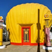 The Last Shell-Shaped Shell Service Station, a bright yellow building designed like a giant seashell, with two vintage pastel gas pumps and a red door