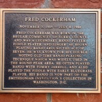 A commemorative plaque honoring Fred Cockerham, legendary banjo and fiddle player from Surry County. The text highlights his early start in music, his distinctive double noting banjo technique, and his collaborations with Tommy Jarrell. It also mentions that his banjo is now part of the Smithsonian Institution's collection