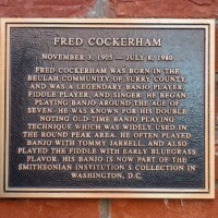 A commemorative plaque honoring Fred Cockerham, legendary banjo and fiddle player from Surry County. The text highlights his early start in music, his distinctive double noting banjo technique, and his collaborations with Tommy Jarrell. It also mentions that his banjo is now part of the Smithsonian Institution's collection