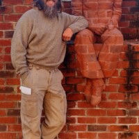 A playful moment at The Whittling Wall—one individual blends seamlessly into the brick backdrop in a camouflage outfit, while another stands nearby wearing a red and white striped hat, adding a pop of contrast to the scene.