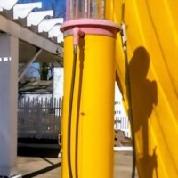 A vintage yellow Shell gas pump with pink accents, featuring a round Shell logo and a glass cylinder used in older models to display fuel levels
